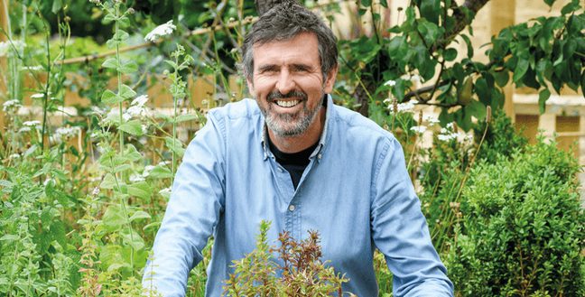 A man in a pale blue shirt stands amongst greenery