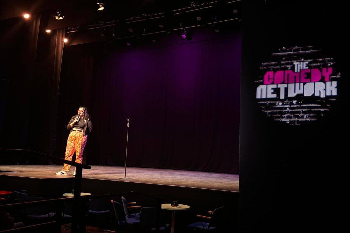 A comedian on stage with 'The Comedy Network' logo to the right of the stage, projected on to the wall