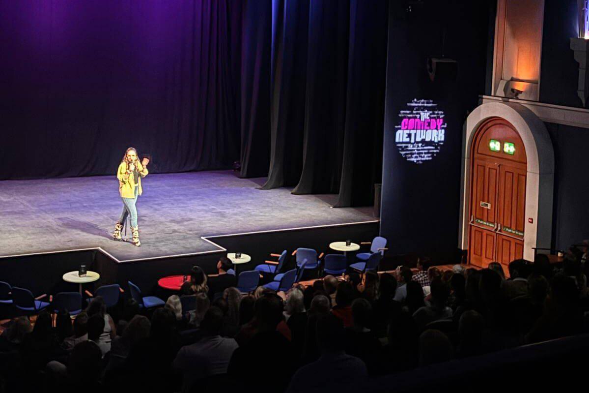A comedian on stage with 'The Comedy Network' logo to the right of the stage, projected on to the wall