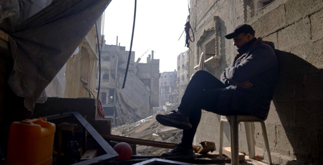 A man sits on a chair in a rubble filled street
