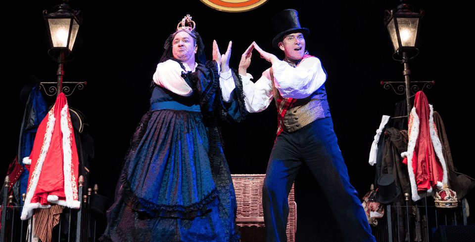 Two people on stage, one wears a crown and one wears a top hat