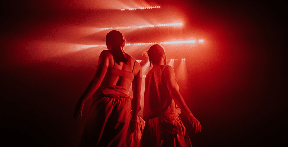 Two dancers walk towards strips of bright red light