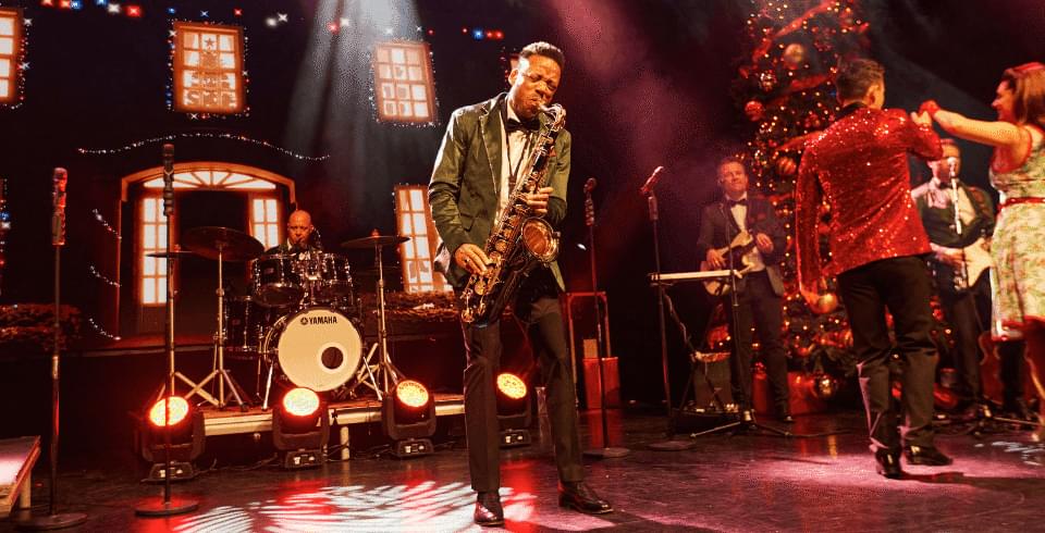 A man in a gold suit jacket plays into the saxophone on stage