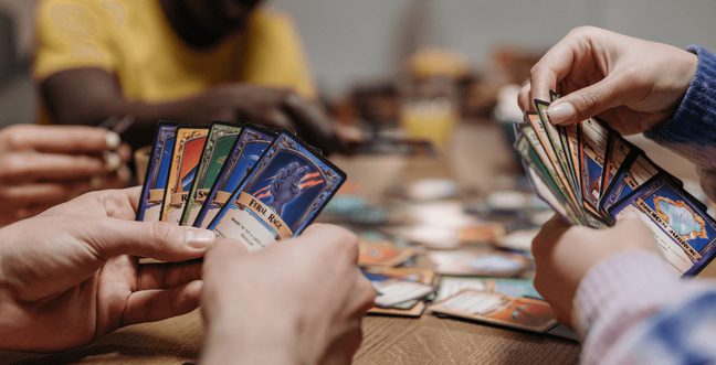 A group of people sit around a wooden table playing a card game