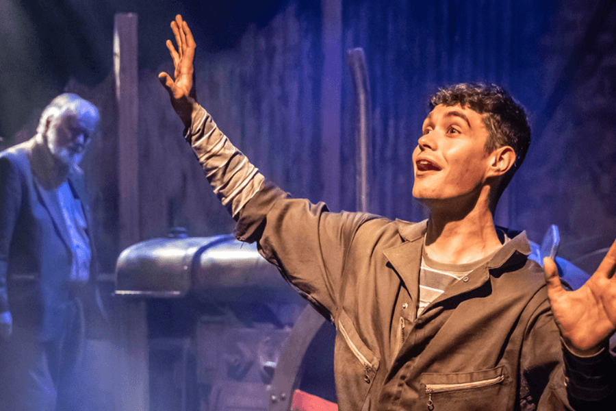 A young man with his arms outstretched in front of a blue light with an elderly man in the background