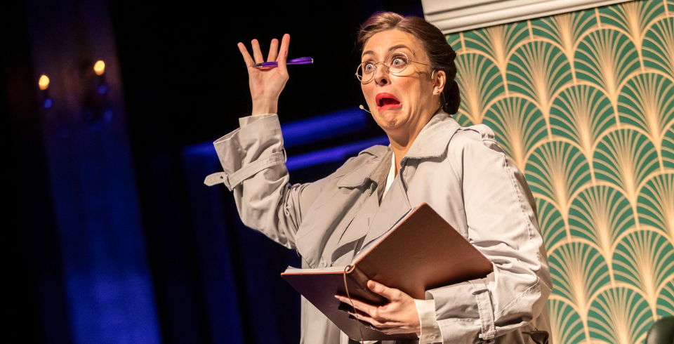 A woman with red lipstick holds one hand in the air in shock while holding a book