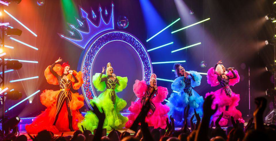 A group of performers on stage singing in multi coloured outfits