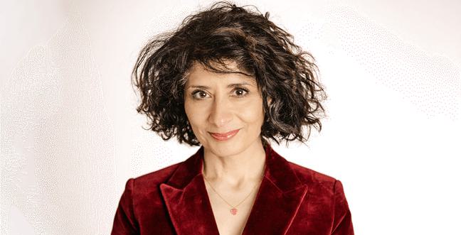 A woman with wild brown wavy hair, wearing a red velvet blazer, smiles