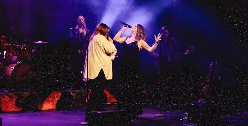 Two performers on stage singing passionately into microphones