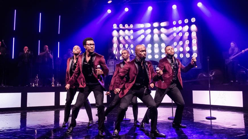 A group of men on a purple-lit stage with burgundy suits