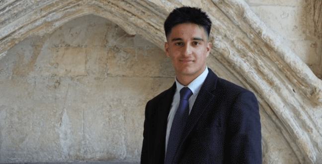 a young man in a suit and tie stood in front of a stone wall with and archway