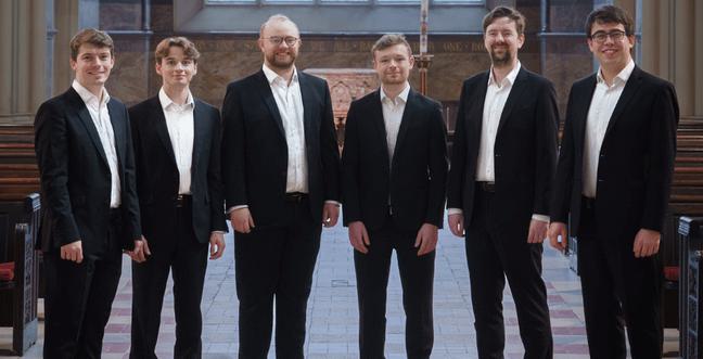 6 men in suits stood in a line in the aisle of a church hall