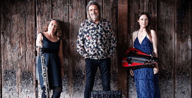 A tall man stands between two women while they all pose against a wooden paneled wall