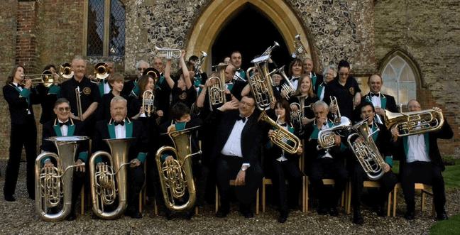 A large brass band stand together outside in a group holding their instruments