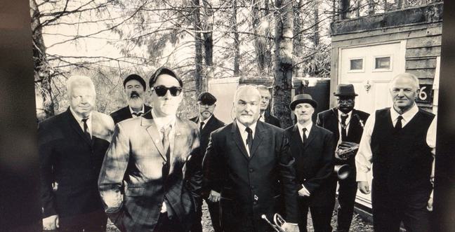 A large group of men in suits stood in a sunny woodland setting