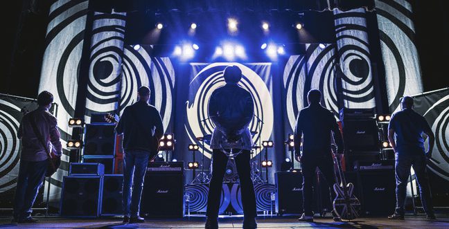 A silhouette of a band on stage backed by a projection of black and white psychedelic spirals