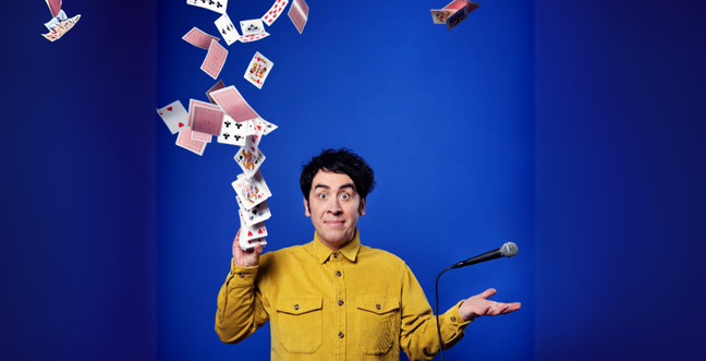 A man with brown hair and a yellow shirt throws a deck of cards in the air