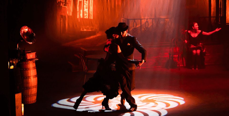 A couple dance in low red lighting by a decorative light projected on the floor