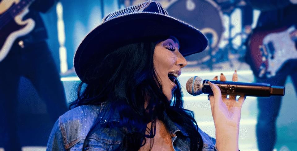 Cher wearing a black cowboy hat singing into a microphone