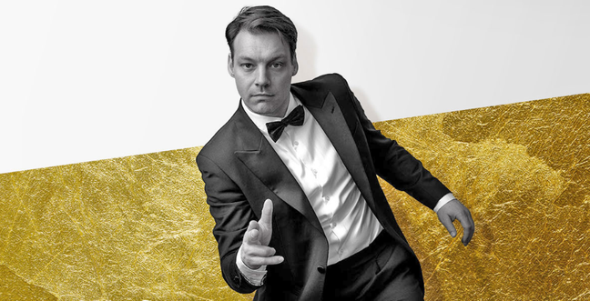 A man in black and white pointing his fingers at you as if shooting a gun. He wears a tuxedo with bow tie.