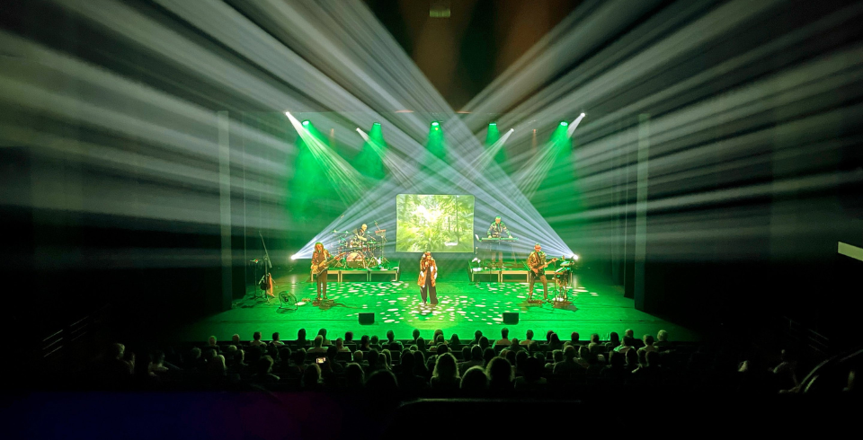 Green lights shoot out from the stage filling the room with beams of light as a band perform on stage