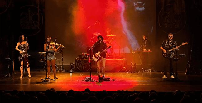 Lit by a red spotlight, a band play on stage together