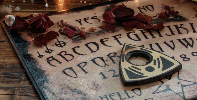 A wooden Ouija board with rose petals on it