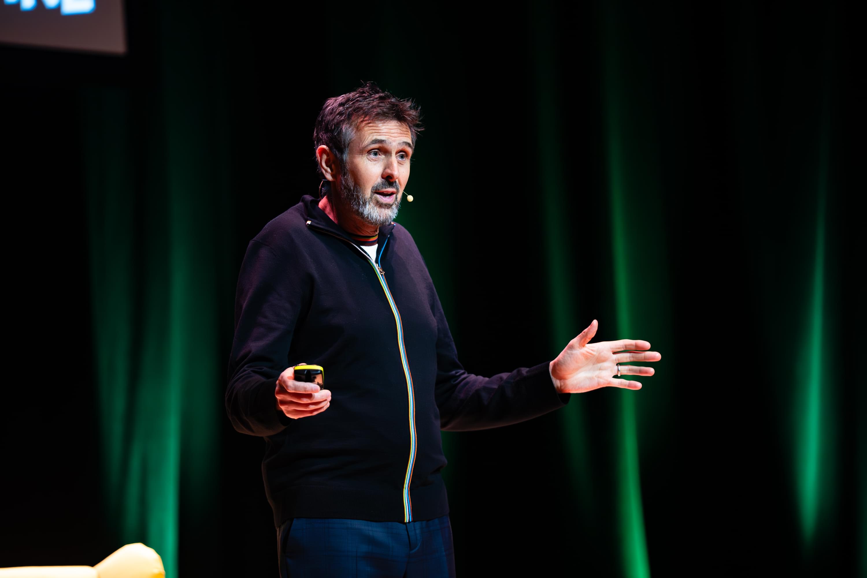 A man in front of a green curtain on stage with a small microphone