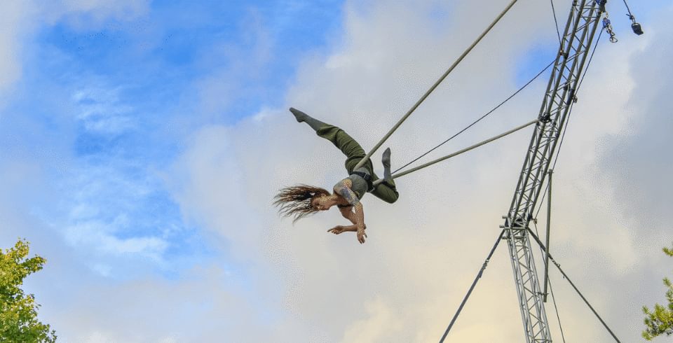 A woman hangs mid-air on a rope with blue cloudy sky behind her
