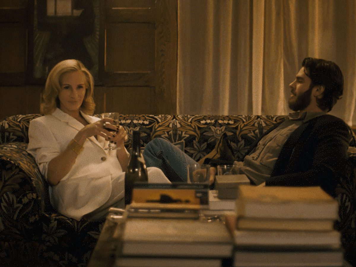 A woman with a white top and blonde hair sits on a pattern sofa next to a man