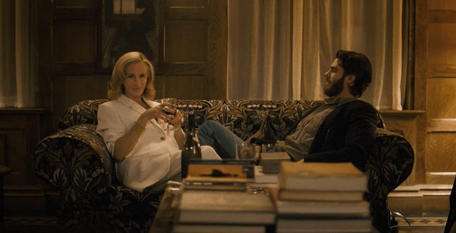 A woman with a white top and blonde hair sits on a pattern sofa next to a man