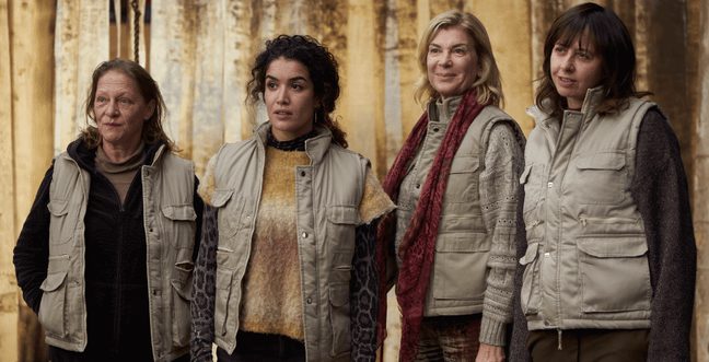 A group of four women stand together in a forest with beige gilets