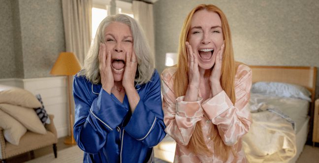 Two women in pyjamas stand in a bedroom screaming with their hands on their faces