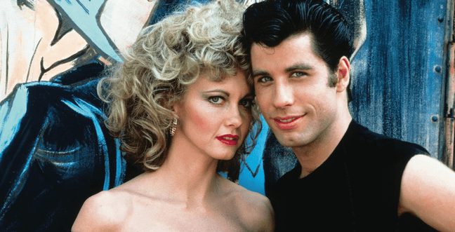 A man wearing black clothes and a woman with curly hair stood close together in front of a painted wall.