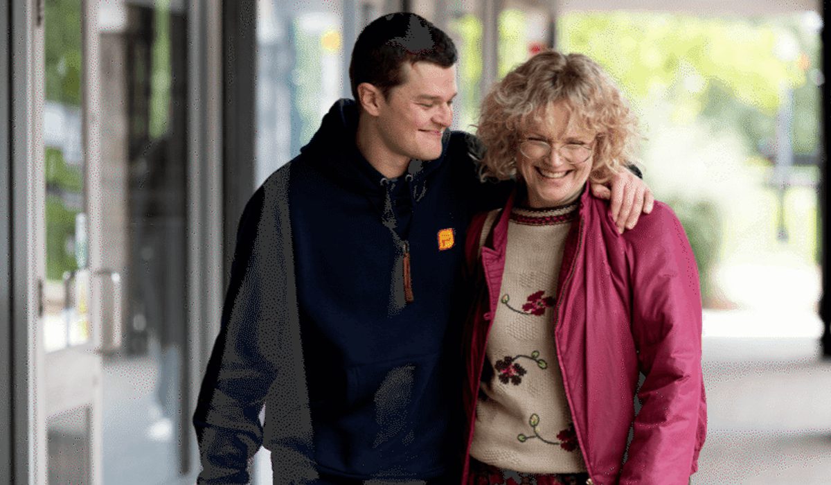 A man holds the shoulder of a woman with a pink jacket, walking down a street
