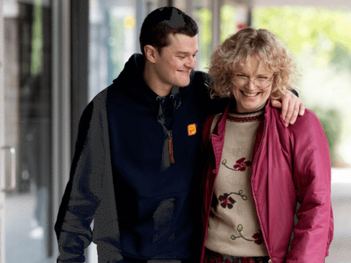 A man holds the shoulder of a woman with a pink jacket, walking down a street