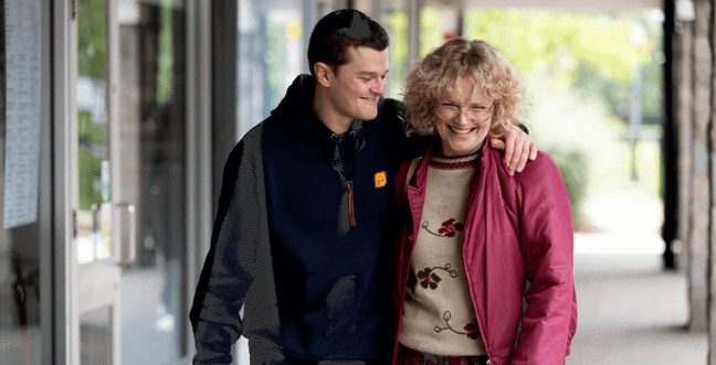 A man holds the shoulder of a woman with a pink jacket, walking down a street