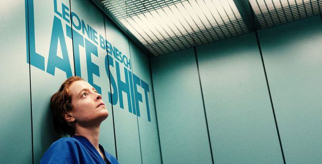 A nurse stands in their scrubs in a lift looking at the ceiling