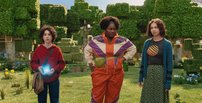 Two women and a young boy stand in a green forest made up of digital cubes