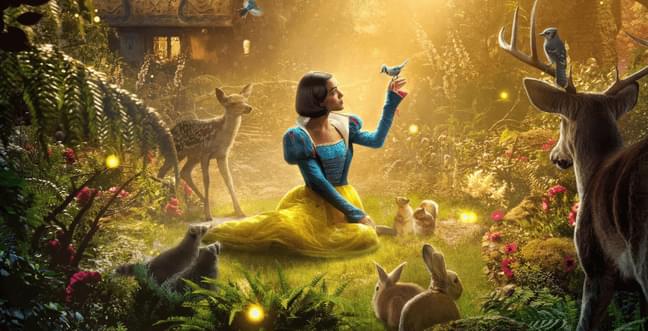 A woman sat in a woodland clearing wearing a blue and yellow dress with short black hair. She is surrounded by woodland creatures like rabbits and deer and has a small blue bird sat on her hand