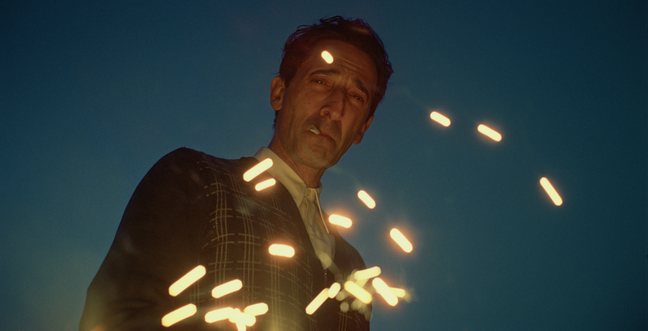 A man in the darkness with a cigarette in his mouth looks down with bright sparks in front of him