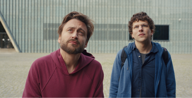 Two brown haired men, one in a red shirt and one in a blue shirt, stare at something in the distance