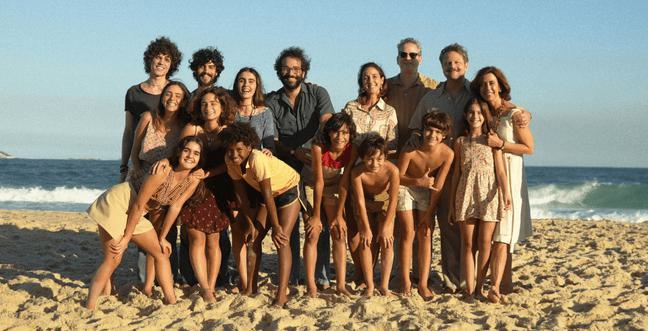 A group of people huddle together in the sun in front of the sea on the beach