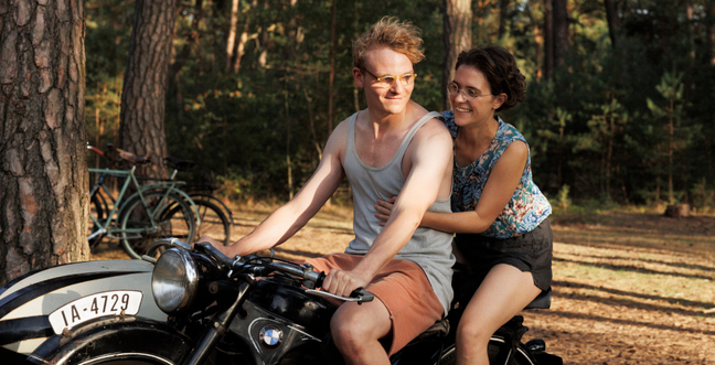 Two people sit on a motorbike in the countryside