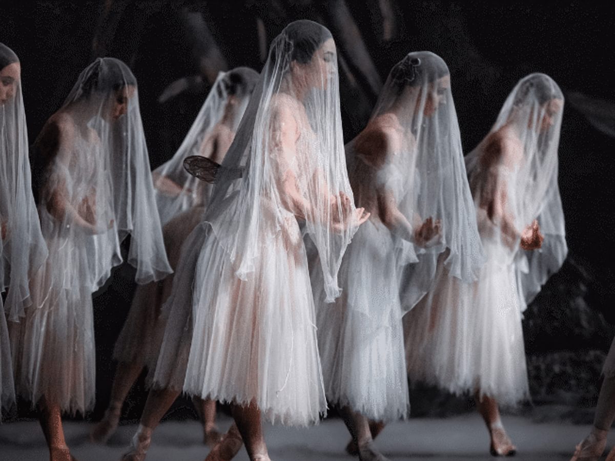 A group of female dancers all dressed in white and wearing sheer veils over their faces.