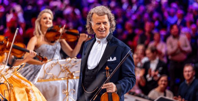 Andre Rieu holds a violin in front of a large crowd