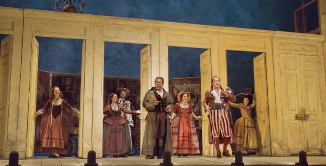 A group of people on stage in front of a large set with doors stand in each doorway