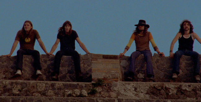 A group of men sit on a stone wall with a blue dark sky behind them
