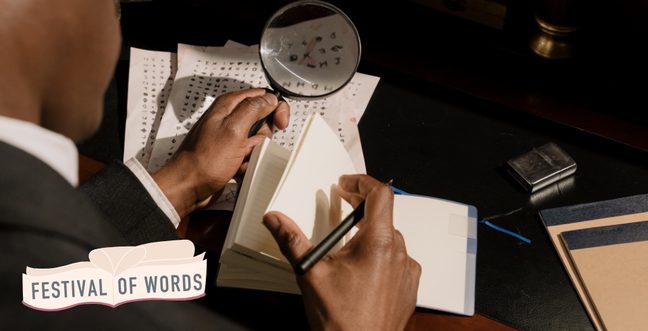 A man in a suit flips though a notebook while holding a magnifying glass