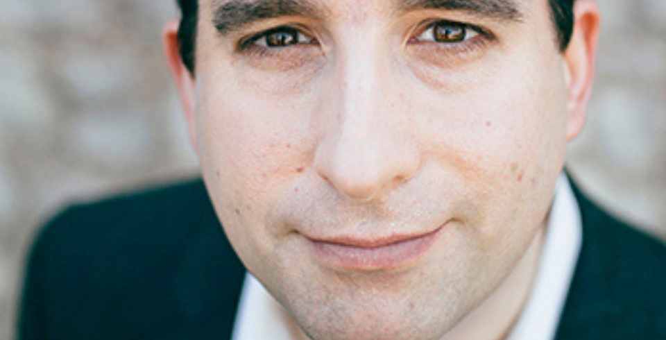 A man with short brown hair wears a suit